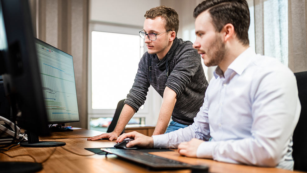 Zwei Projektmanager beraten sich vor dem Computer anhand eines Projektzeitplans.
