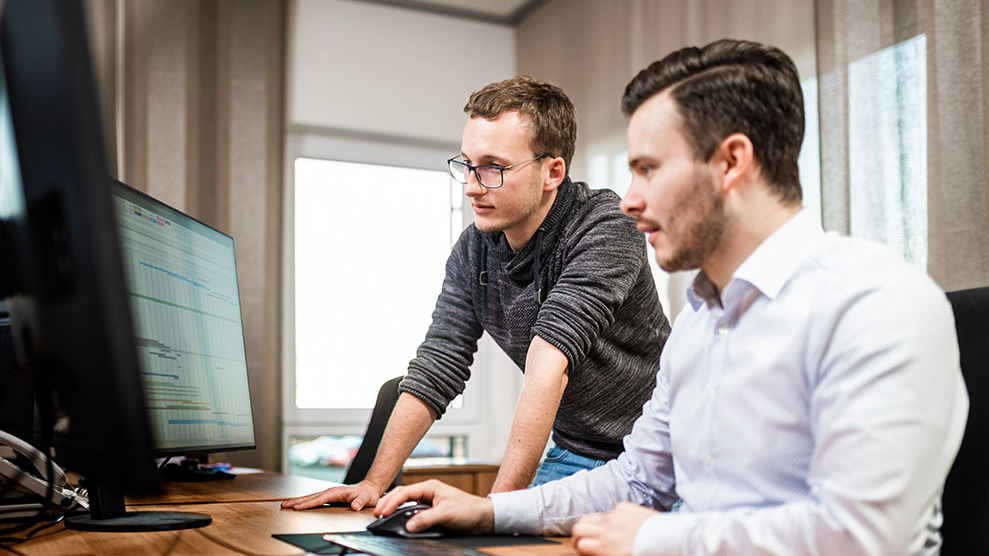 Zwei Projektmanager beraten sich vor dem Computer anhand eines Projektzeitplans.